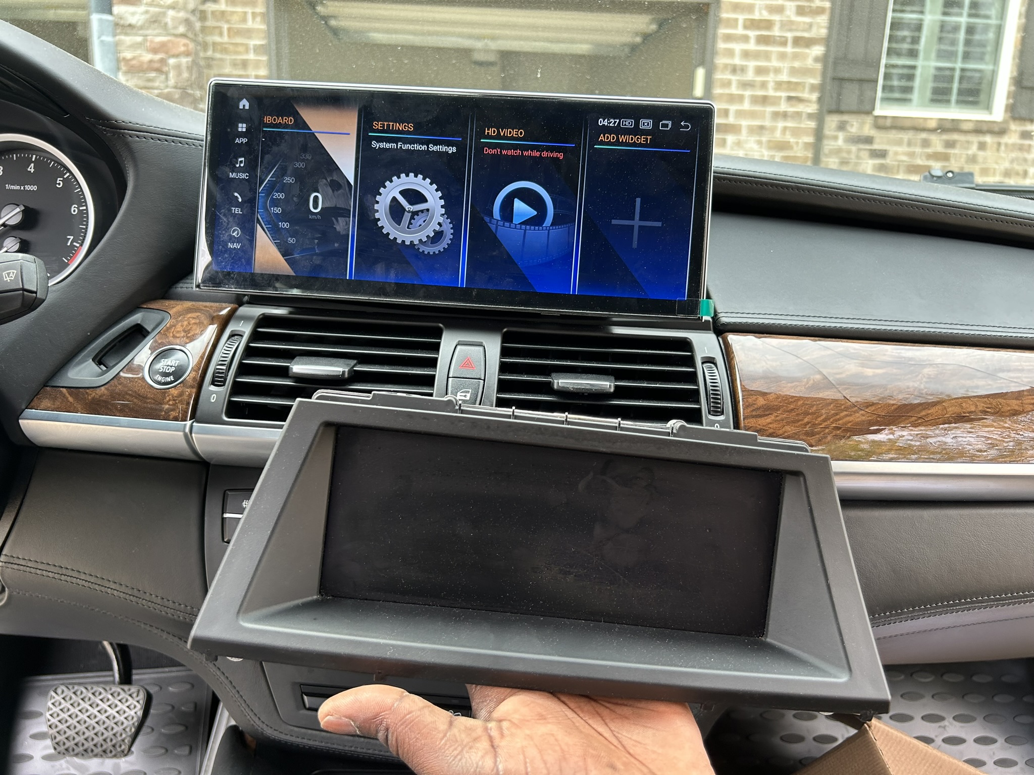 BMW X5 dash with a wide Android CarPlay screen installed, old iDrive display held in front