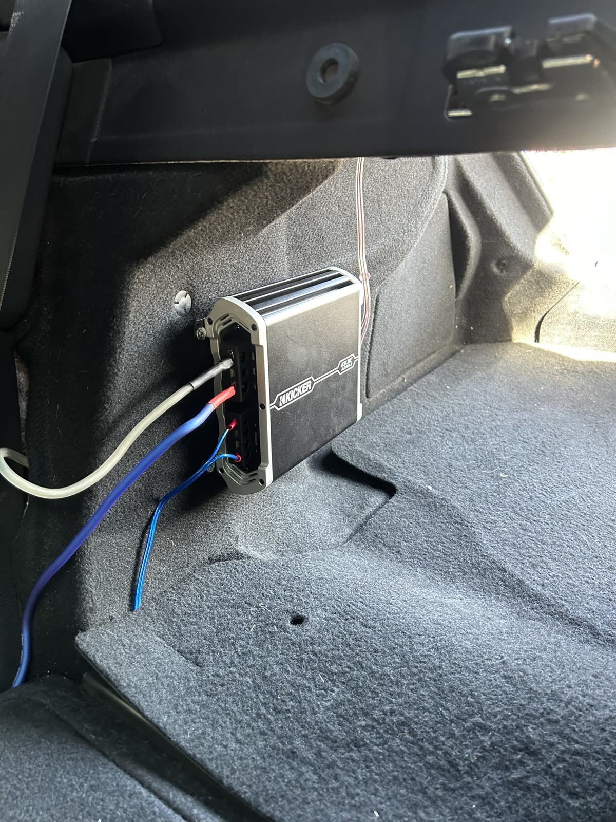 Compact Kicker amp mounted on the trunk side wall with power and signal wiring run to it